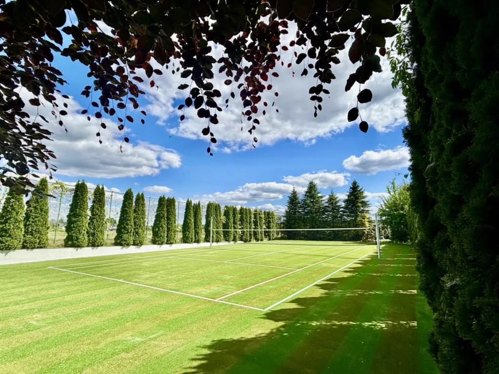 Prywatny kort tenisowy – wielofunkcyjne boisko do tenisa, badmintona, siatkówki i mini futbolu, otoczone zielenią.