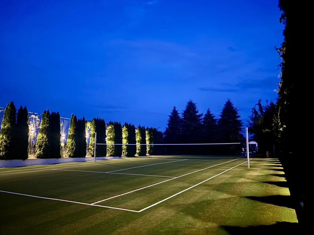 Prywatny kort tenisowy – wielofunkcyjne boisko do tenisa, badmintona, siatkówki i mini futbolu, otoczone zielenią.